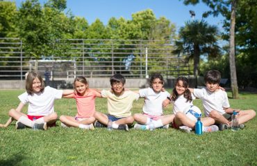 Children sitting together in a park, smiling and enjoying a sunny day outdoors.